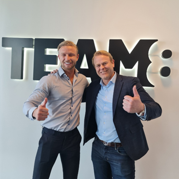 En bild på ägarna av 2 företag framför loggan som tillhör team8.
