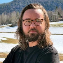 Joakim Karsberg står i naturen med glasögon på sig.